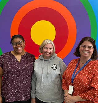 Three happy teachers in front of color wheel on wall